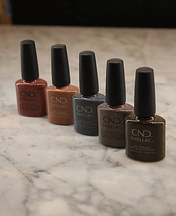 Cinco esmaltes CND Shellac en tonos de otoño, de óxido a café oscuro, alineados sobre mármol.