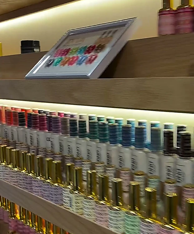Repisas de madera iluminadas, llenas de frascos de esmalte de todos los colores, con una carta de tonos arriba.