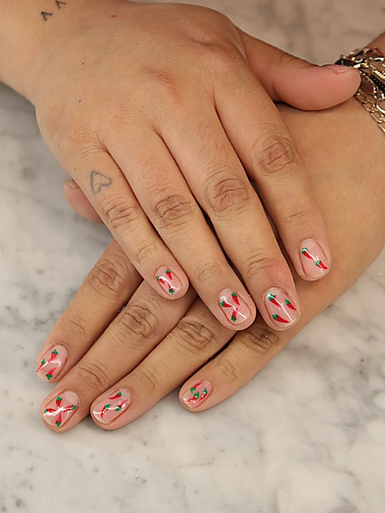 Manos sobre mármol con uñas cortas en tono nude decoradas con chiles rojos y verdes pintados a mano.