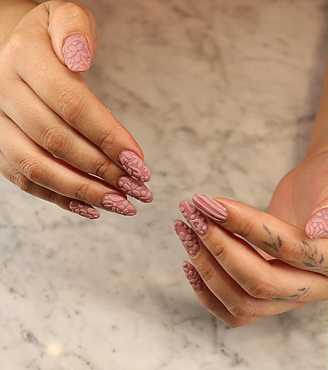 Uñas largas almendradas en rosa empolvado con efecto suéter en relieve, sobre mármol.
